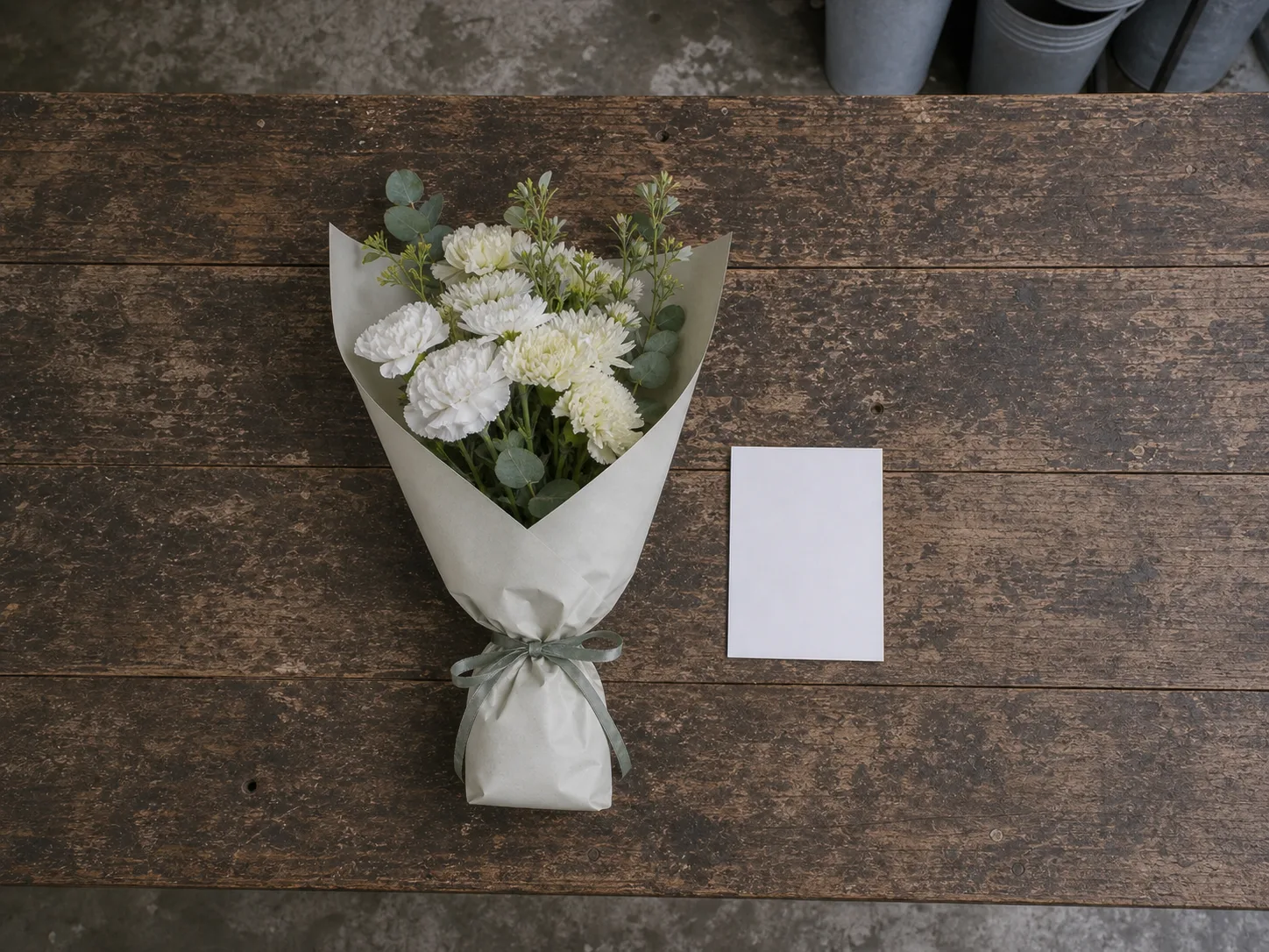 A small bouquet of white carnations, cream chrysanthemum and pale green foliage lying wrapped on the shop bench
